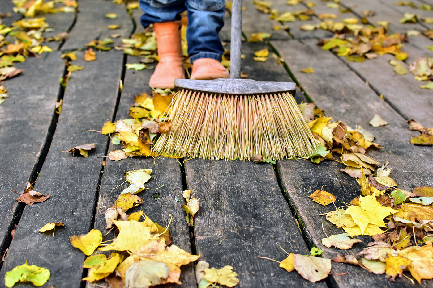 Person using a broom to sweep off autumn leaves on wood deck.